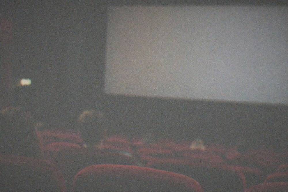 Dimly lit cinema auditorium with rows of red seats facing a blank screen