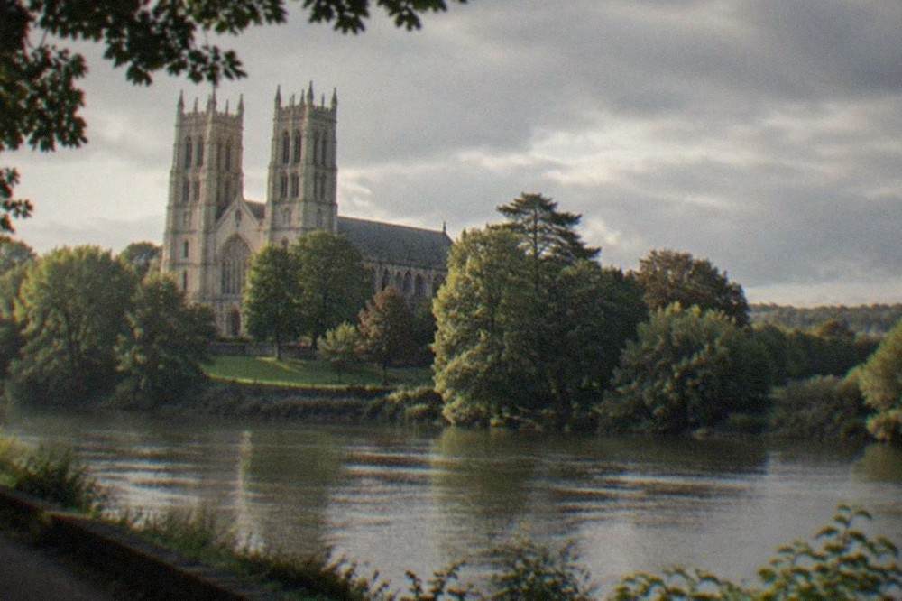 A Gothic cathedral tower rising above trees beside a river