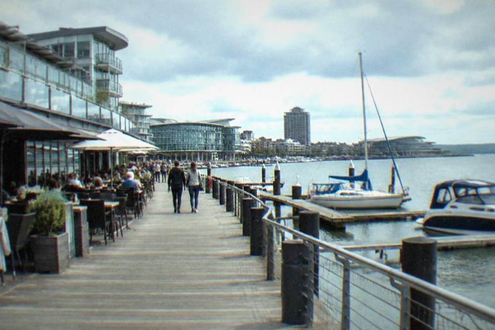 Wooden boardwalk beside moored boats with diners at outdoor tables