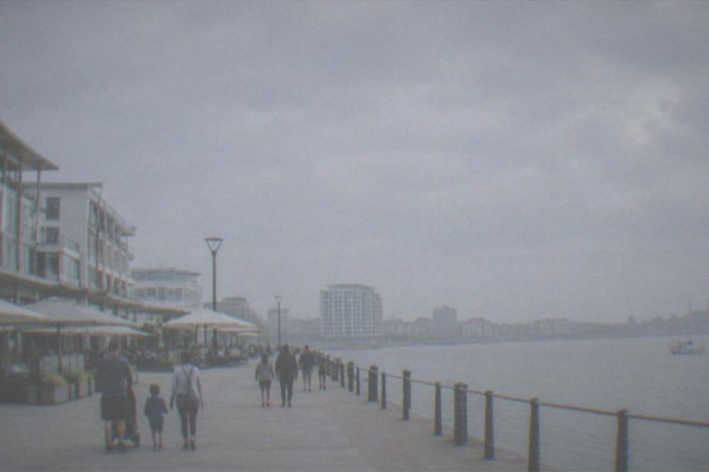 Families walking along a wide waterfront plaza beside a large building