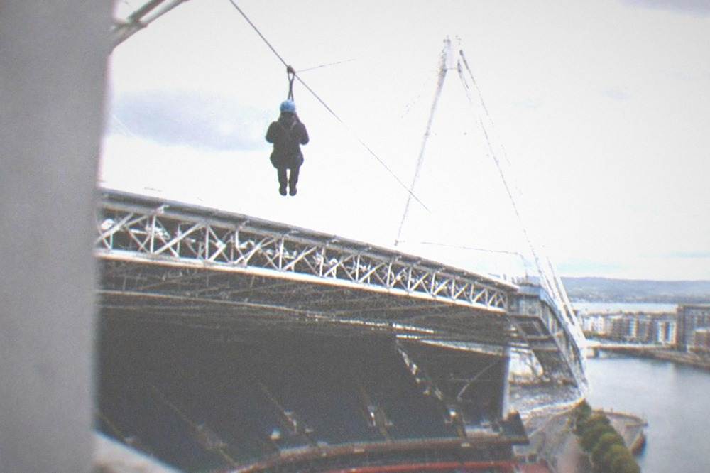 A person on a zip line harness high above a stadium seating bowl