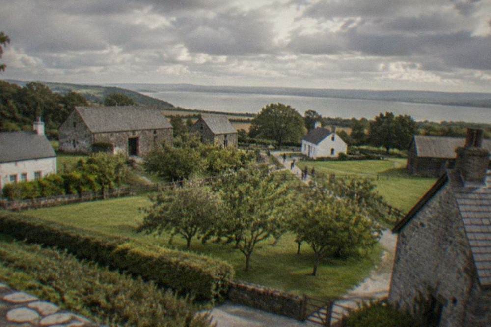 Historic stone buildings arranged across an open-air museum lawn under a wide sky