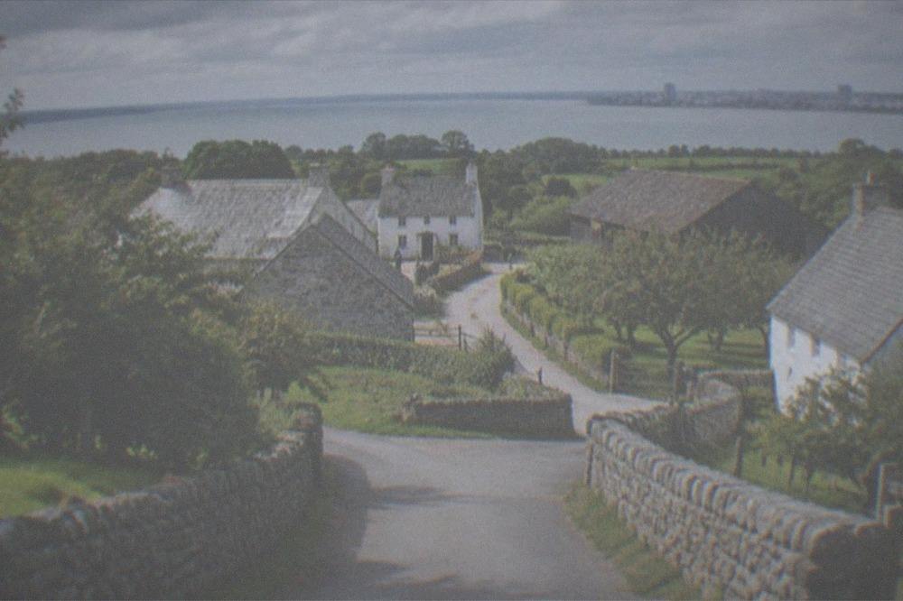 A quiet country lane approaching a stone museum entrance on a mild afternoon