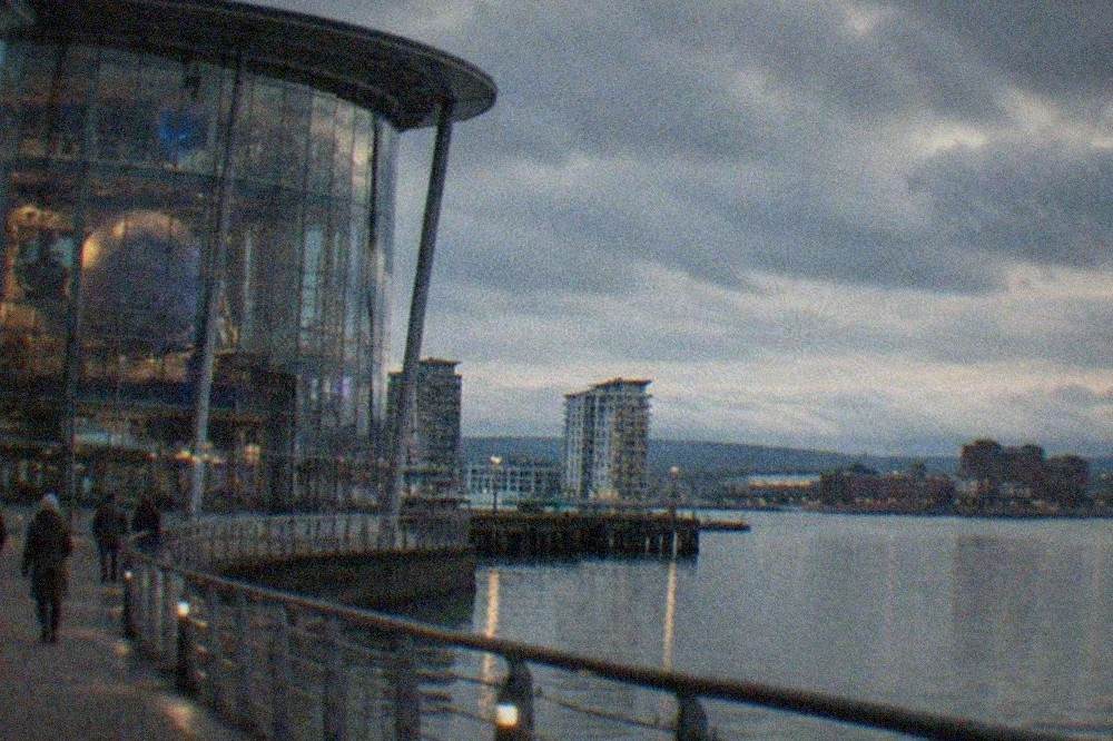 Glass-fronted science centre building on a Cardiff Bay street with water beyond