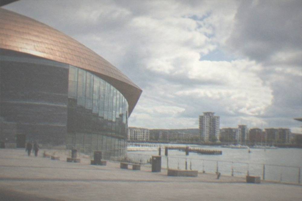 A calm waterfront lake with boats moored and buildings along the shore