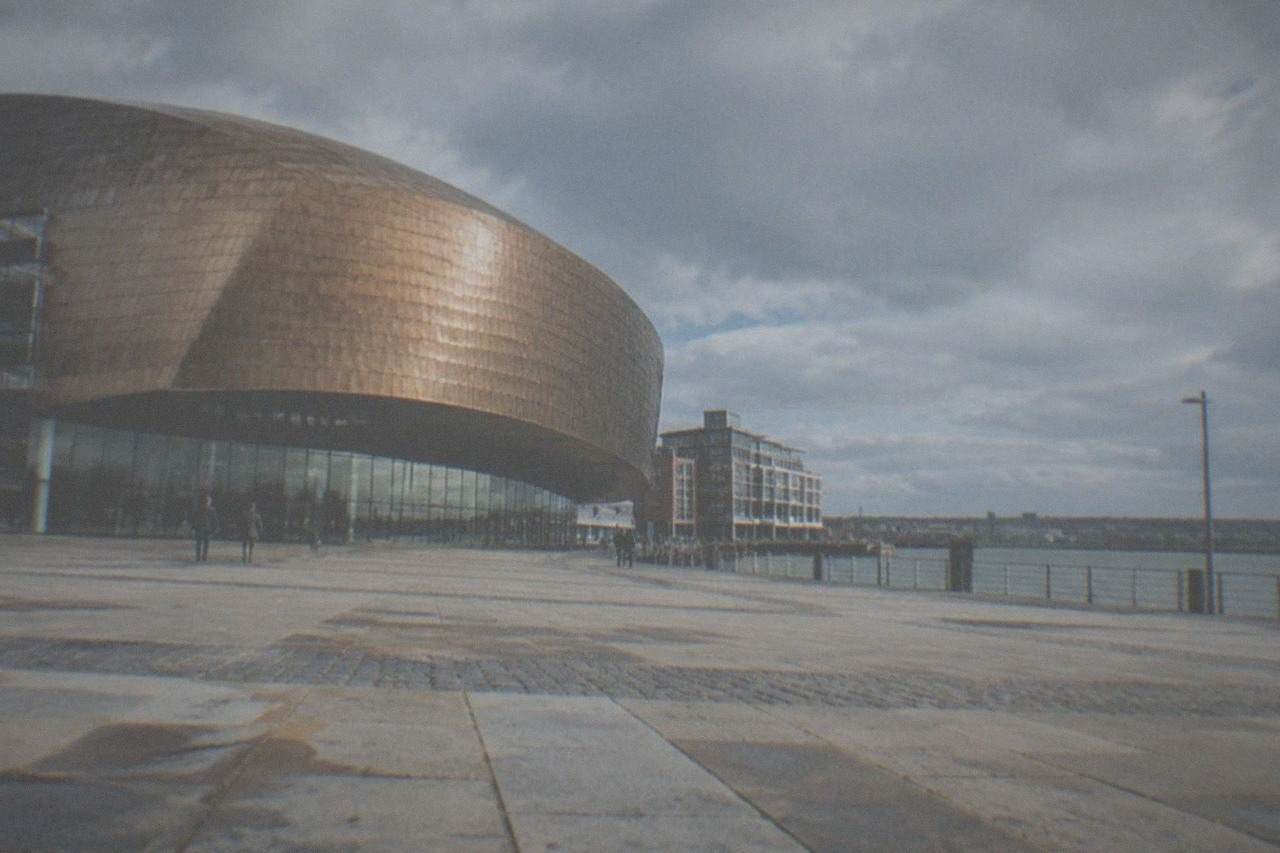 The bronze facade of a large waterfront arts centre under a wide sky