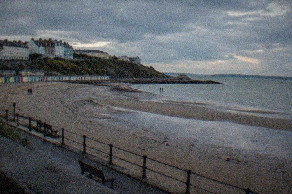 A sandy beach at low tide with a promenade and colourful beach huts behind it