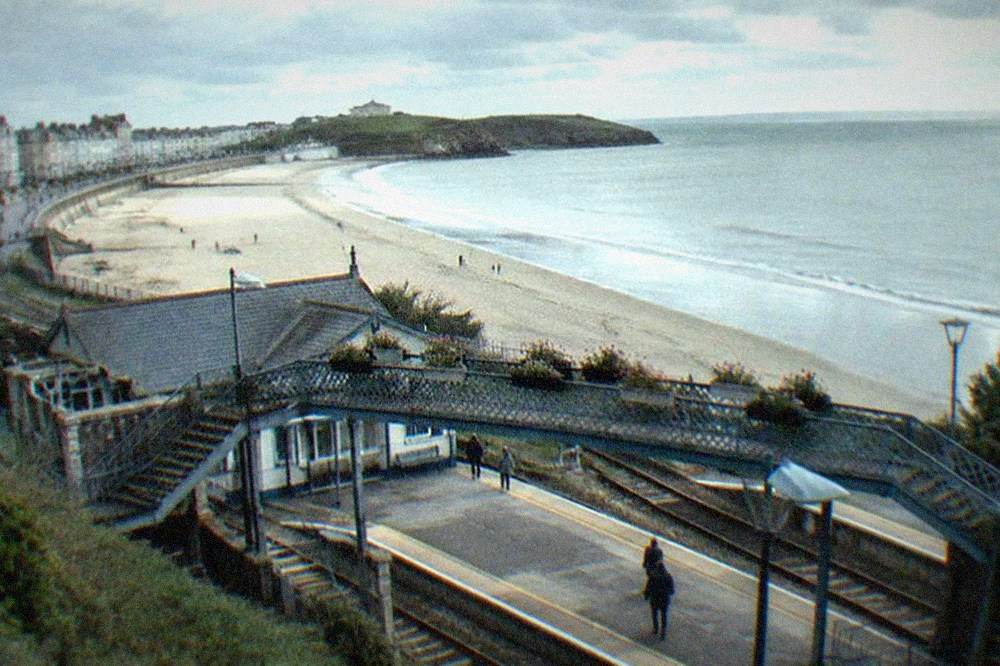A small seaside railway station with a footbridge and flower planters