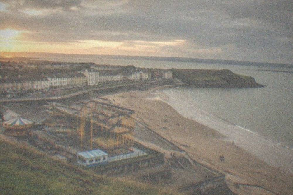 A fairground with a rollercoaster and rides above a beach and sea wall