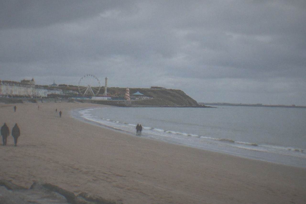 A wide sandy beach beside a small seaside town with a pleasure park and a calm sea