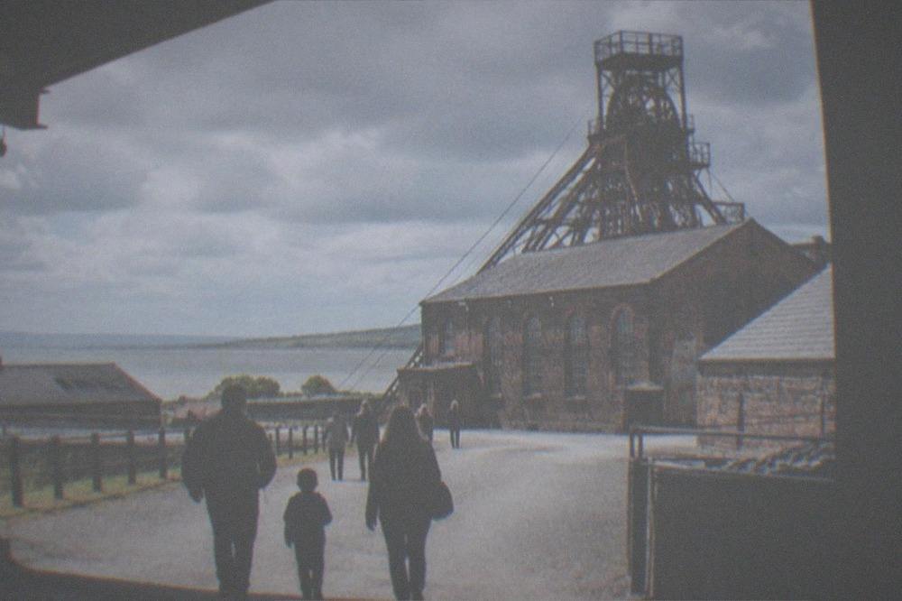 Family walking a colliery yard path towards a brick winding tower