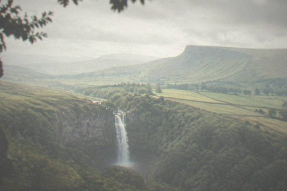 A tall waterfall dropping into a wooded gorge in waterfall country