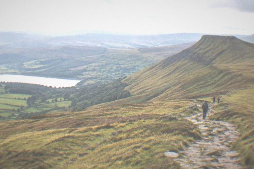 A stone path climbing across open grassy slopes toward a rocky summit
