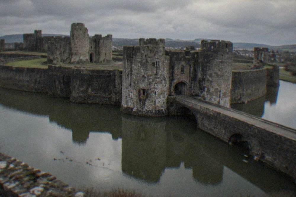 A stone gatehouse reflected in still moat water with wildfowl swimming past