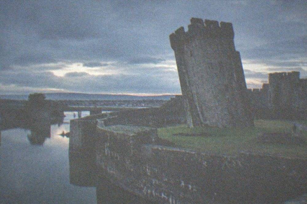 A massive stone tower tilting visibly to one side above a grassy castle courtyard