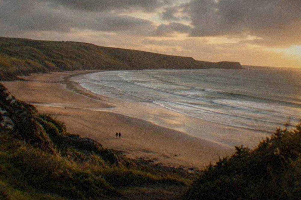 A long curve of golden sand beneath rolling green cliffs with waves breaking softly