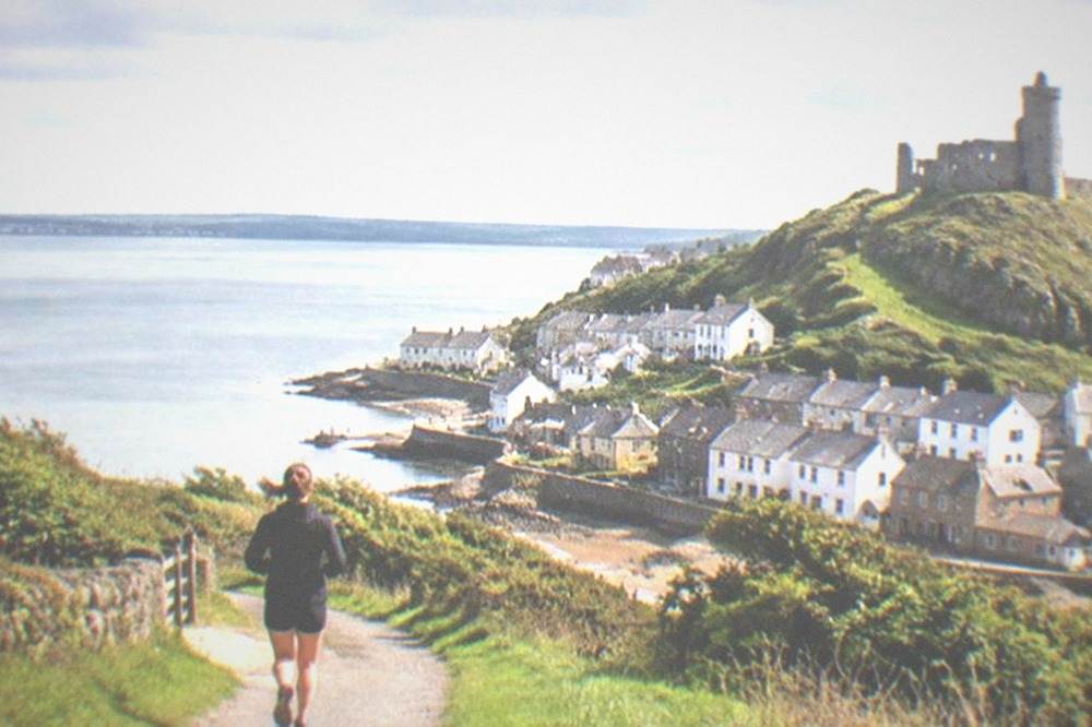 A stone castle tower on a green hill above a small seaside town