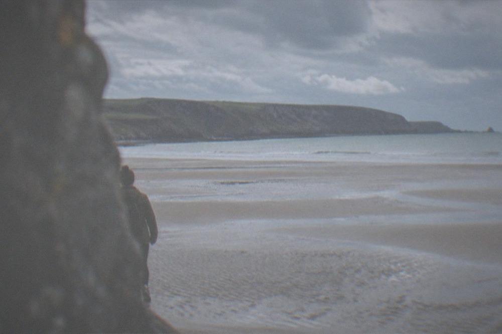 A wide empty beach at low tide with rippled sand and distant cliffs