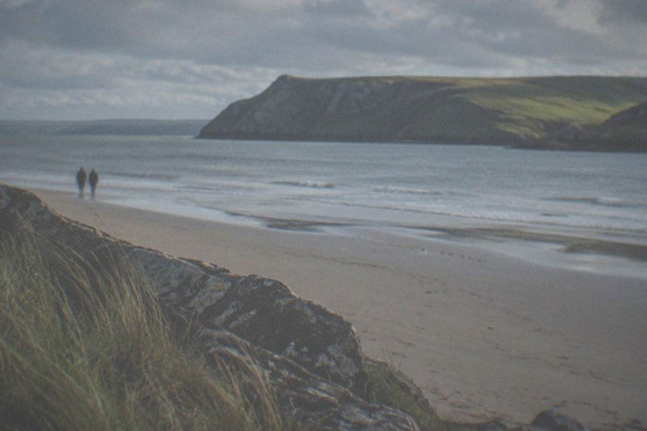 A wide sandy bay backed by grassy cliffs under a bright sky