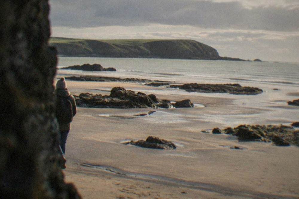 Wide sandy beach at low tide with rock pools and a headland in the distance
