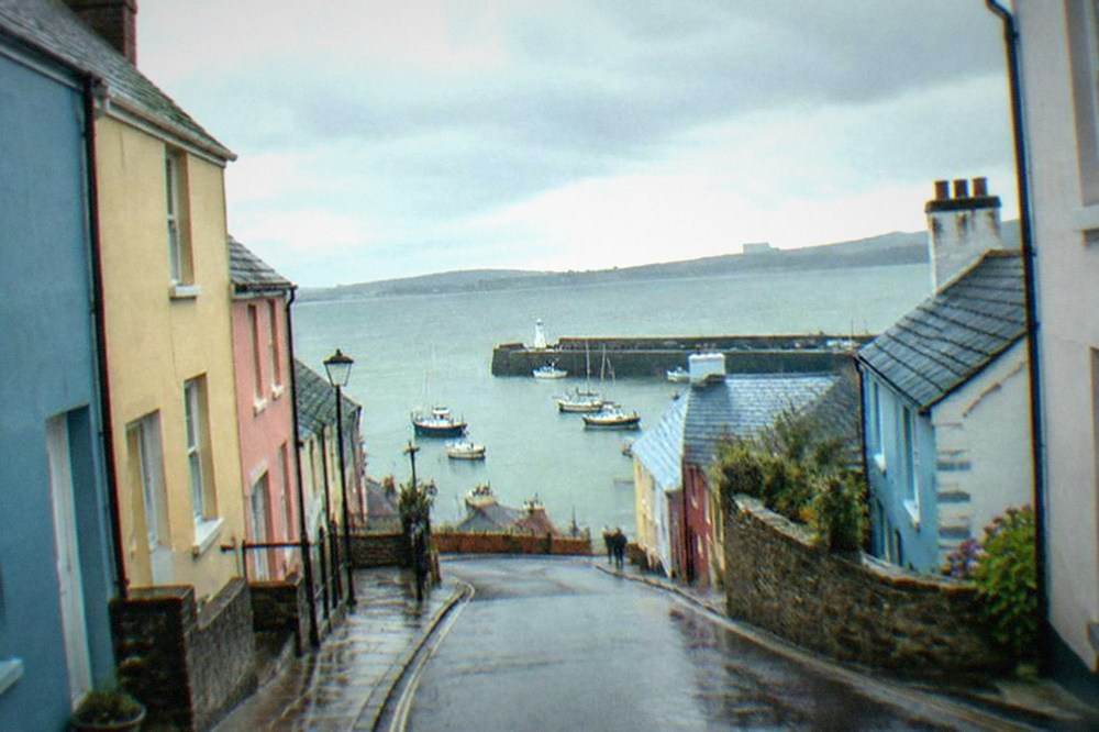 Narrow street of colourful painted townhouses leading down toward a harbour