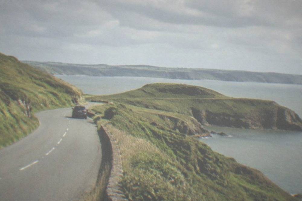 Coastal road curving along a green clifftop with the sea beyond
