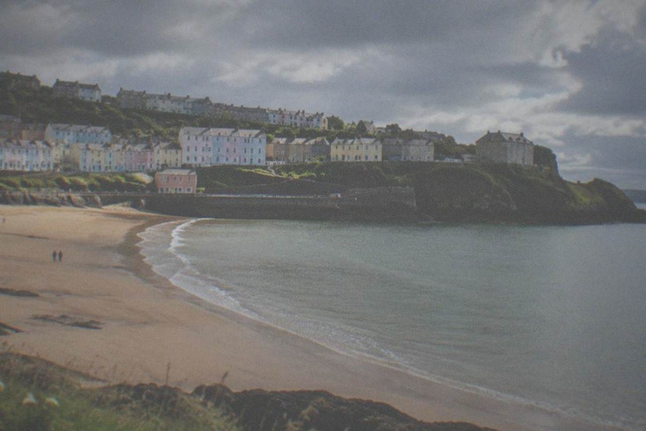 Golden sandy beach below a small coastal town with pastel buildings along a hillside