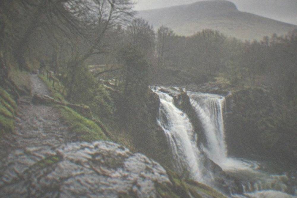 A narrow footpath beside a waterfall dropping through a wooded gorge