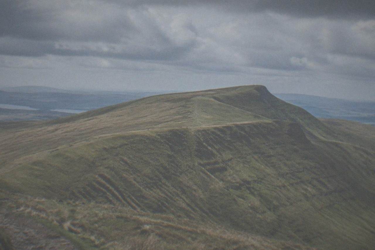 A grassy mountain ridge rising above open moorland under a wide sky
