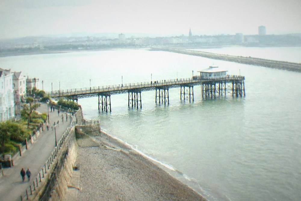 A wide paved embankment path across water towards a town skyline