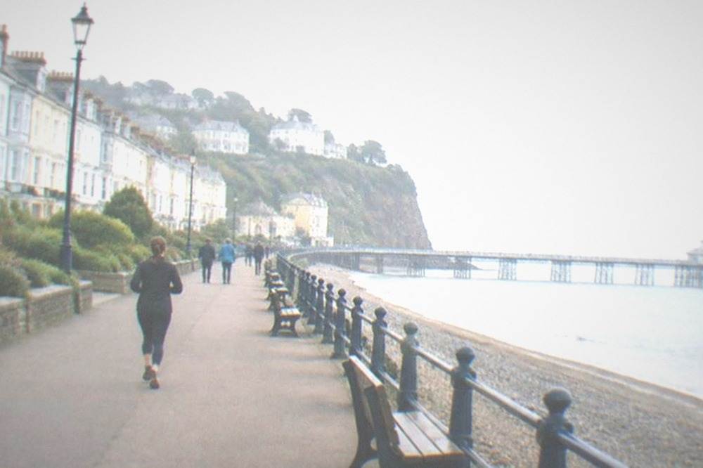 A seaside promenade with benches along a rail and a town on a cliff behind
