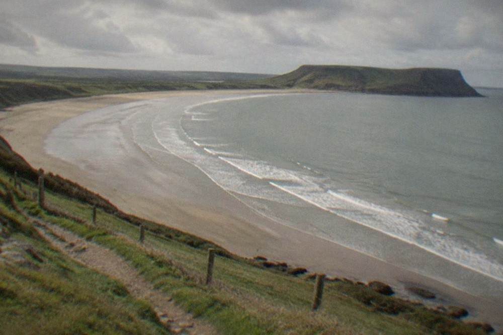 Long curving sandy beach seen from a grassy clifftop path