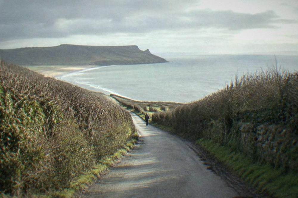 Narrow country lane winding between hedgerows toward the coast
