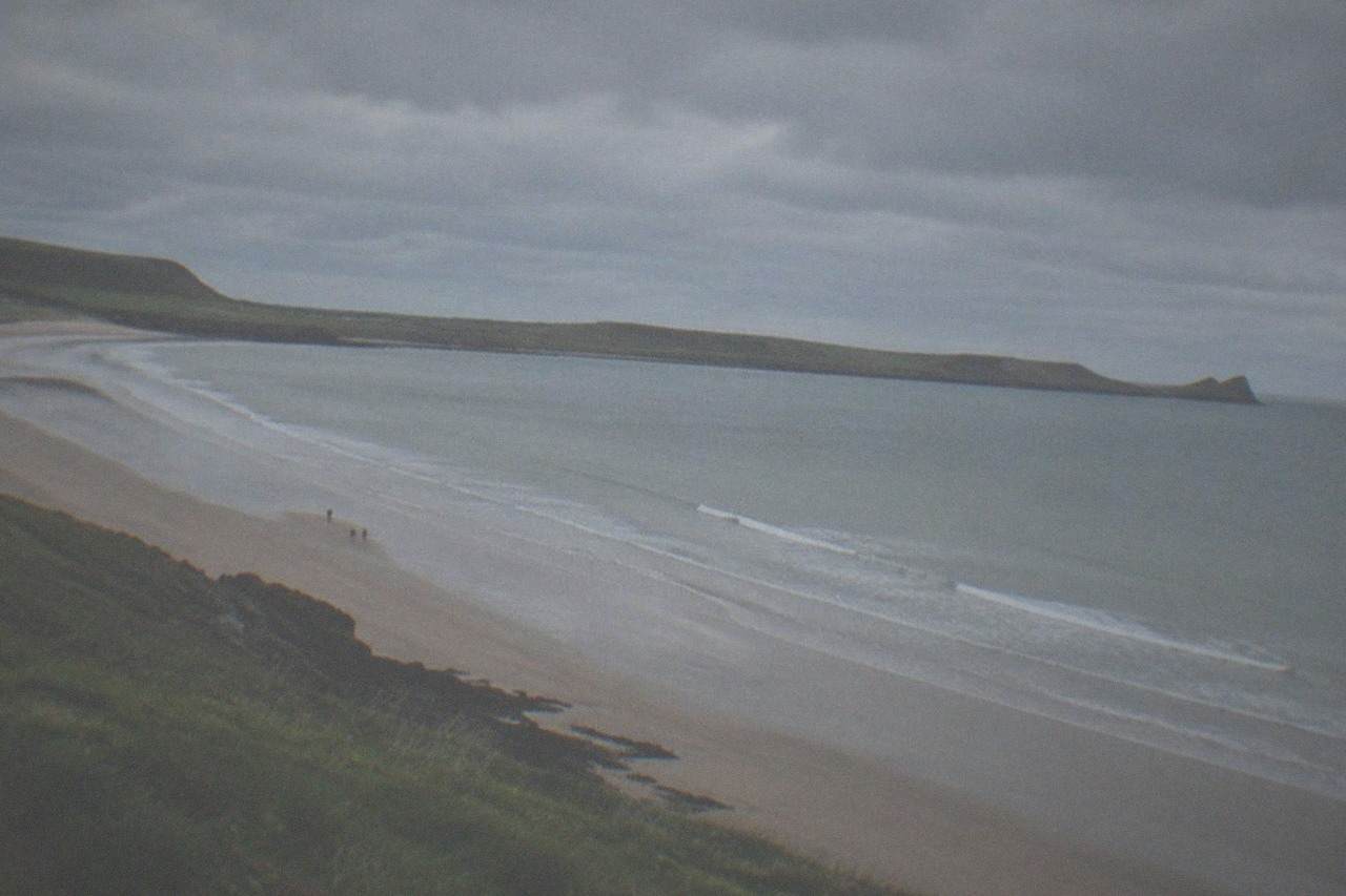 Wide sandy beach curving between grassy headlands under an open sky