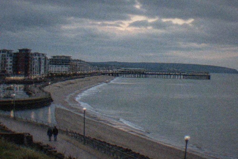 A seaside promenade curving along a bay with a Victorian pier in the distance