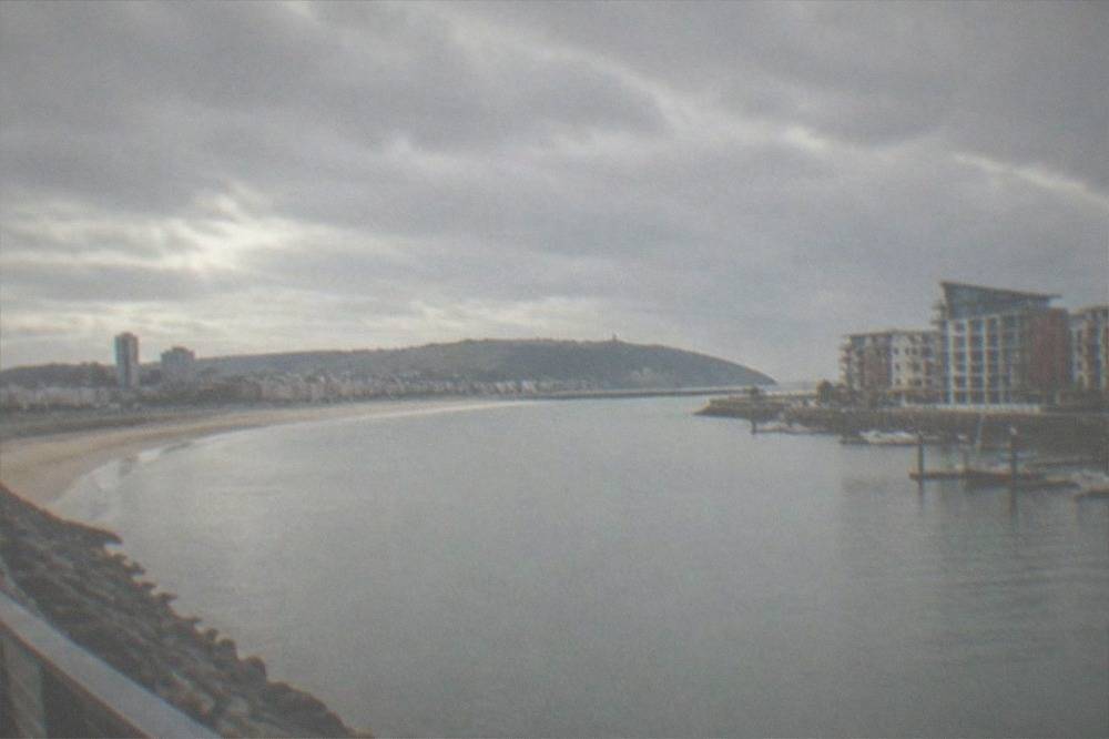 A wide sandy bay curving between a city skyline and green headlands