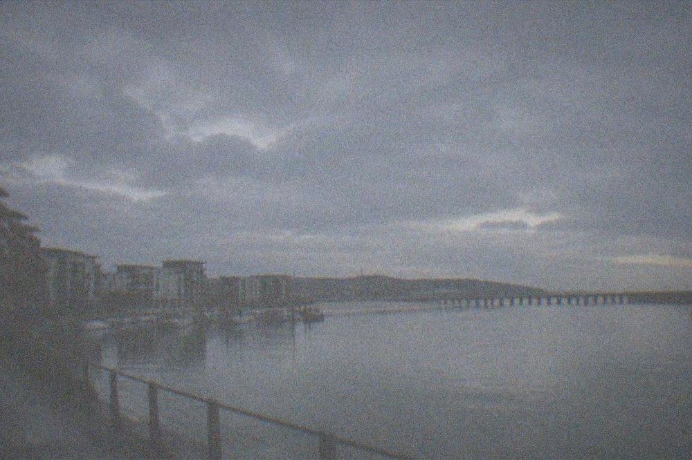 A calm bay at dusk with a long pier silhouetted against the sky