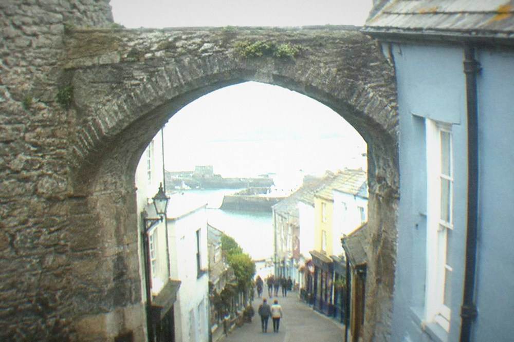 A stone archway in a town wall opening onto a narrow street of shops