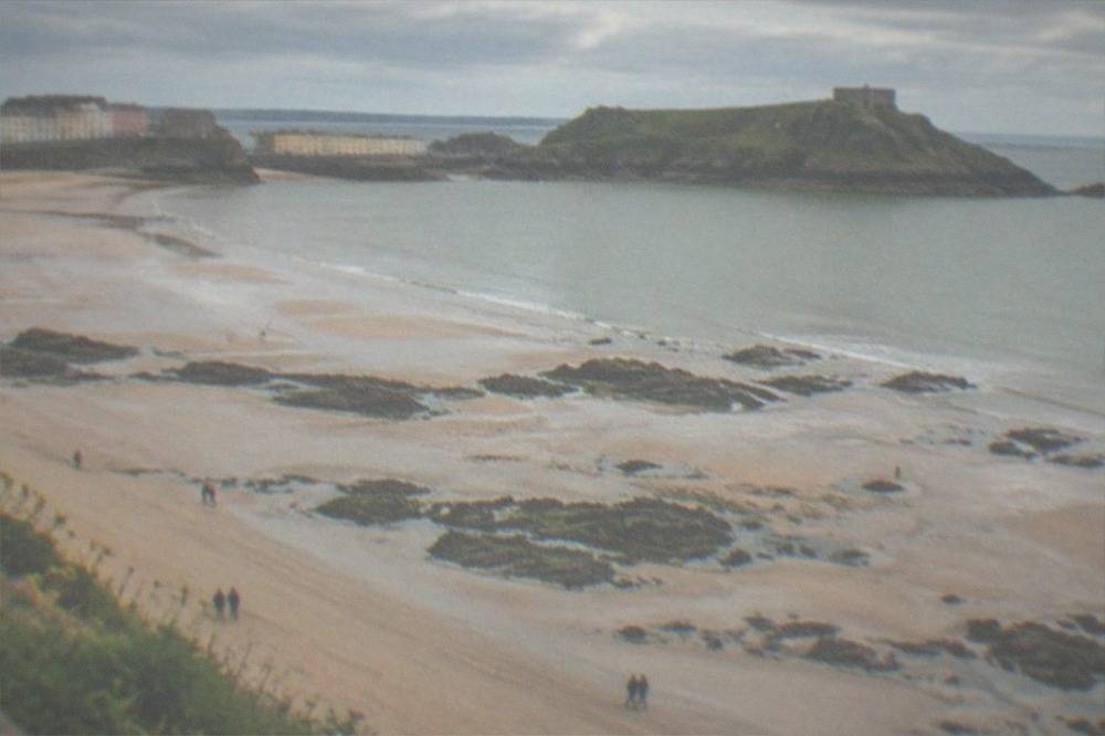 A wide sandy beach at low tide with rock pools and a headland beyond