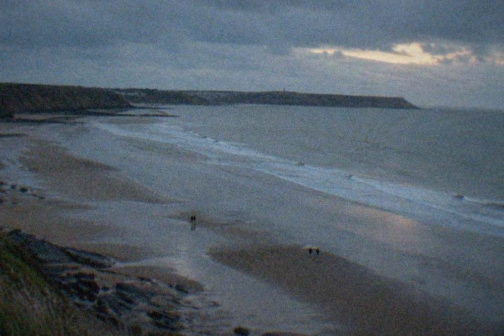 A wide sandy beach at low tide with cliffs in the distance and gentle waves