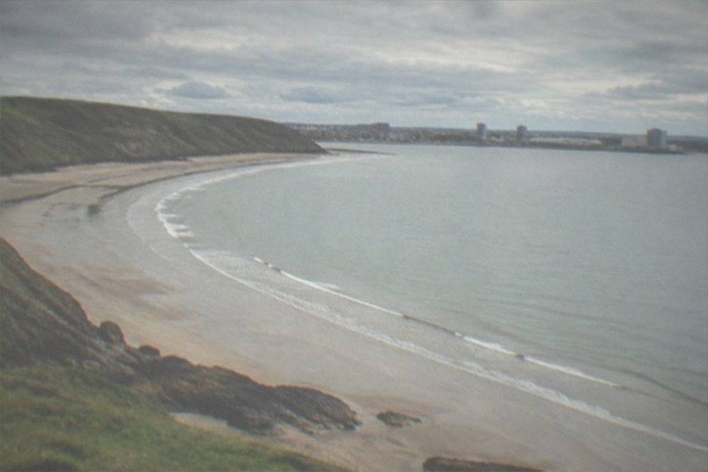 A long sandy bay curving between grassy cliffs under a wide sky