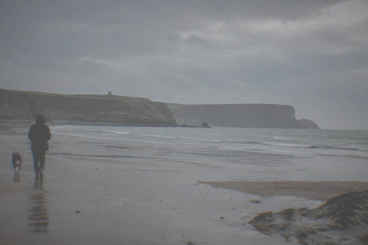 A wide sandy beach at low tide with cliffs in the distance and gentle waves