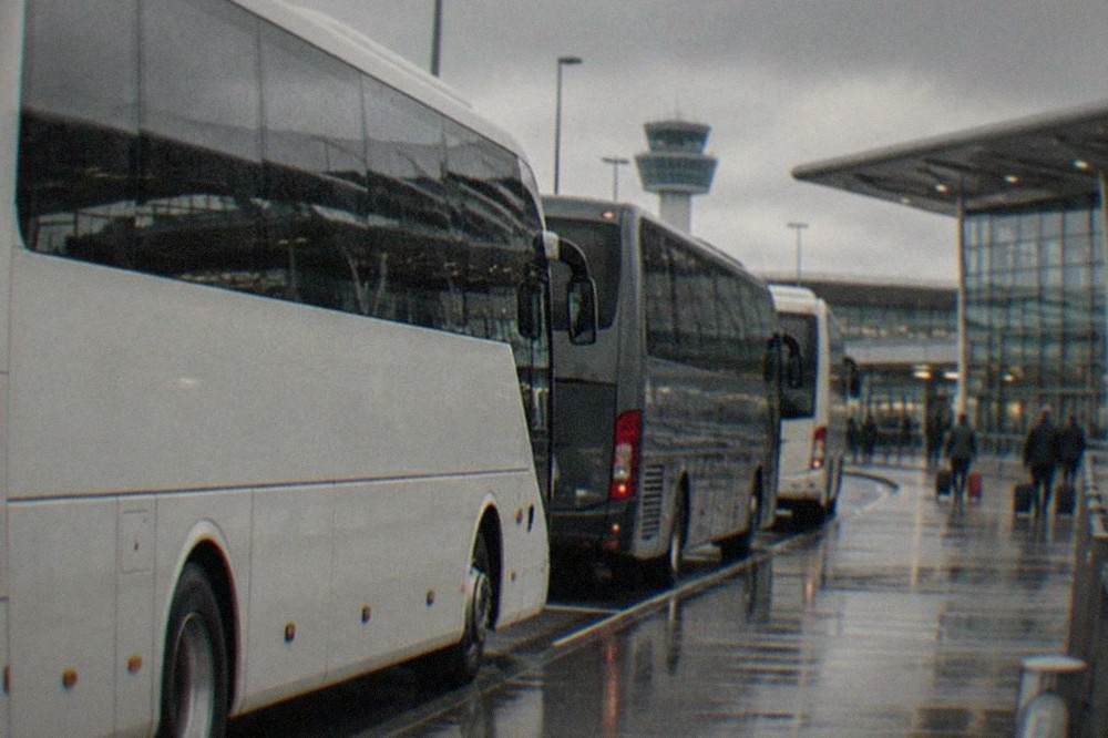 Coaches parked at an airport terminal forecourt under an overcast sky