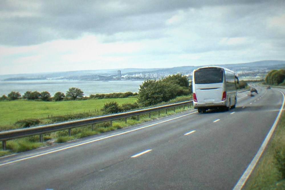 A long-distance coach travelling on a motorway beside green fields