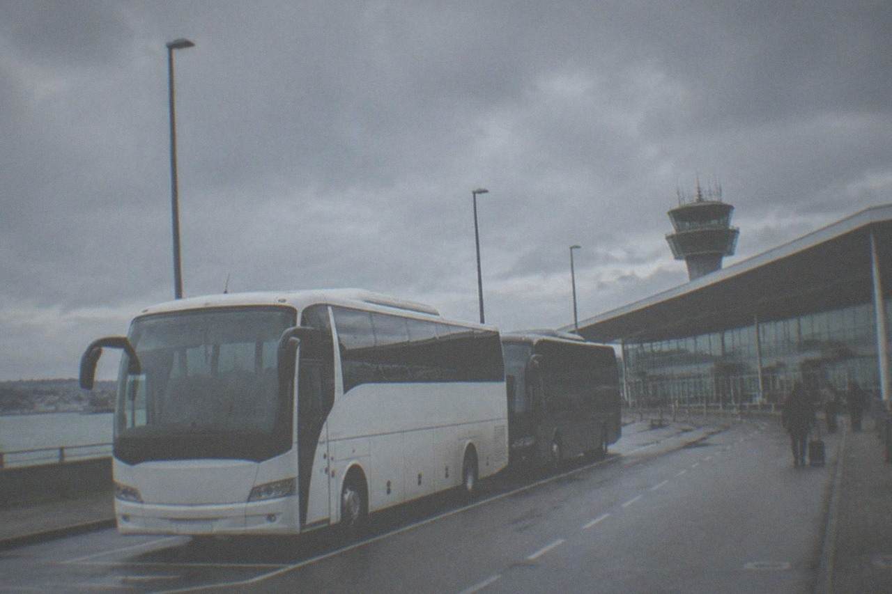 Coaches parked at an airport terminal forecourt under an overcast sky