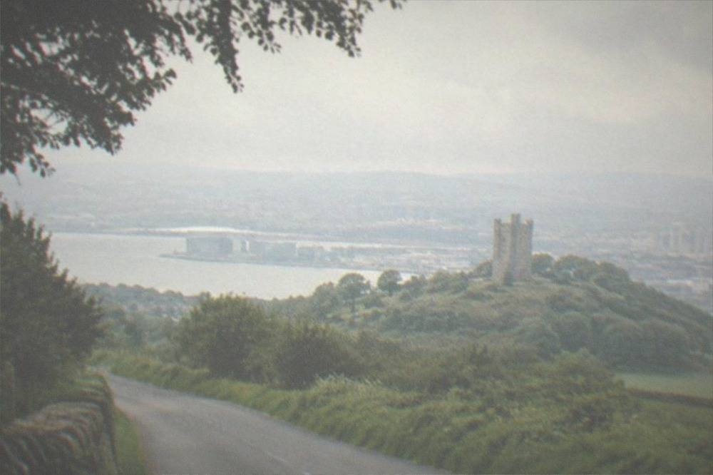 A winding country road through green hills with a castle tower visible in the distance