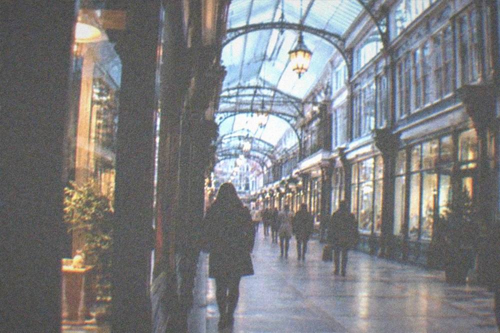 A pedestrian street in central Cardiff with shoppers walking under Victorian arcade glass