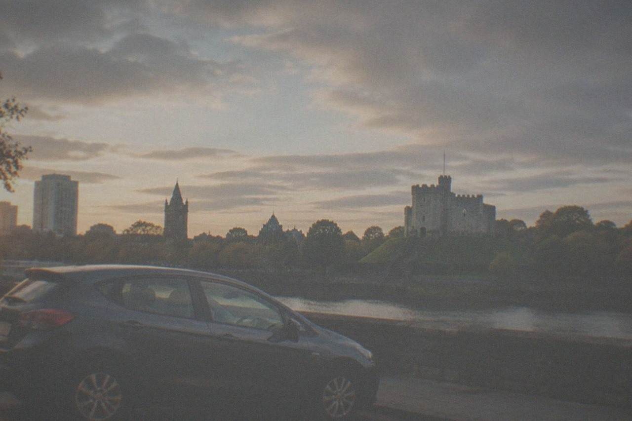 A hire car parked on a Cardiff street with the castle keep rising behind the city skyline