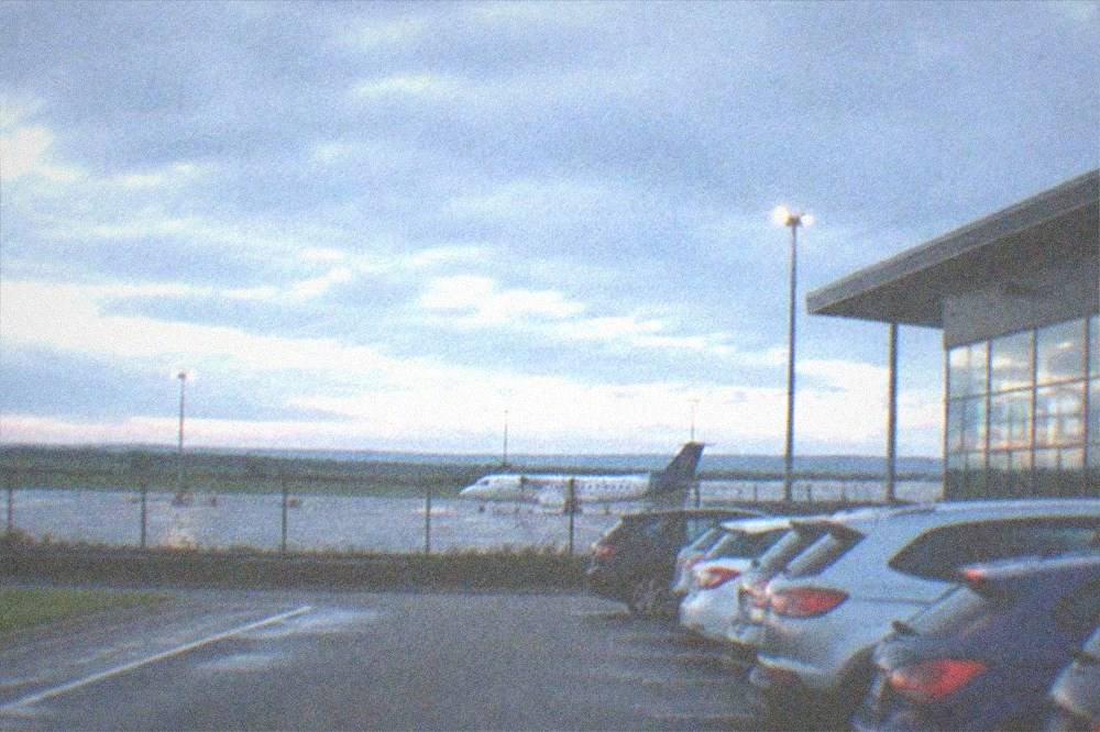 A row of parked hire cars in bays outside an airport terminal