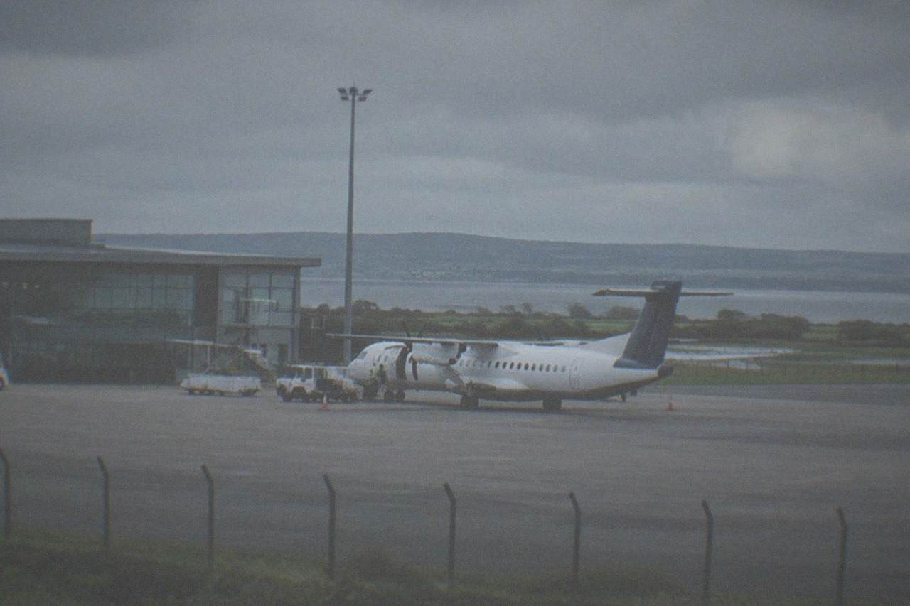 A small regional airport terminal building under an overcast sky with a plane at the stand